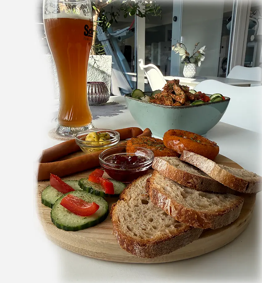 Snack im Römerbad: Weizenbier mit Würstchen hübsch angerichtet auf einem Holzbrett mit diversen Dipps, Brot und Gemüse